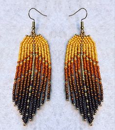 two pairs of beaded earrings with gold and black beads hanging from them on a white surface