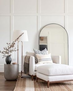 a living room with white furniture and a large round mirror on the wall above it