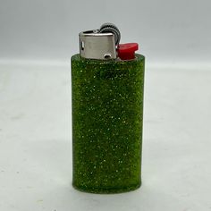 a green flask with a red top on a white table next to a lighter