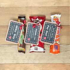 candy bars and snacks are laid out on a wooden table with chalkboard signs attached to them