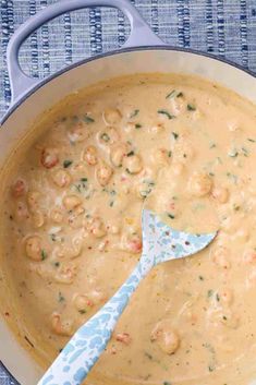 a blue spatula in a white pan filled with shrimp and cheese soup on a table