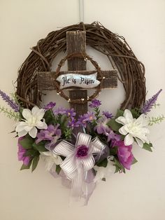 a wreath with purple and white flowers hanging on a wall next to a wooden cross