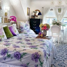 a bed with purple flowers on it in a bedroom next to a dresser and window