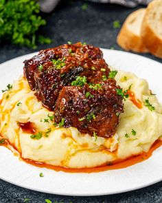 a white plate topped with mashed potatoes covered in meat and gravy next to bread