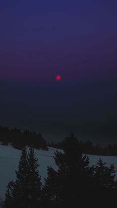 the sun is setting over some trees on a snowy hill with purple skies in the background