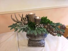 a vase filled with candles sitting on top of a table covered in pine cones and greenery