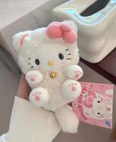 a white hello kitty stuffed animal with pink ears and big paws holding a small card