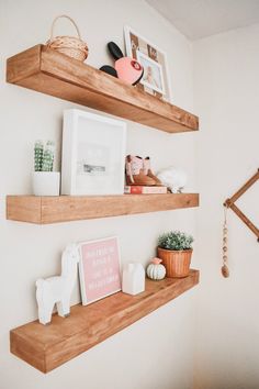 two wooden shelves with pictures and other items on them in a white walled room next to a potted plant