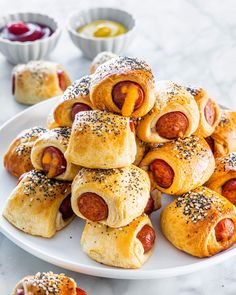 a white plate topped with pigs in a blanket and buns filled with cheese, ketchup and mustard