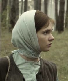 a woman wearing a headscarf standing in the woods looking off into the distance