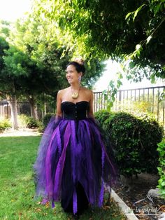 a woman wearing a purple and black dress standing in the grass with her hands on her hips