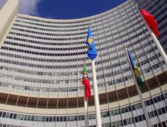 several flags are flying in front of a tall building with many windows on the side