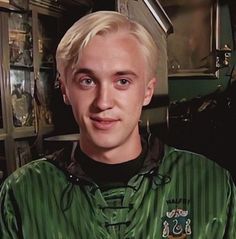 a man with blonde hair wearing a green shirt and looking at the camera while standing in a kitchen