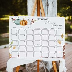 an easel with a guess baby calendar on it sitting in front of a tree