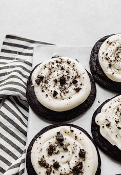 four cookies with white frosting and oreo cookies on a napkin next to a striped towel