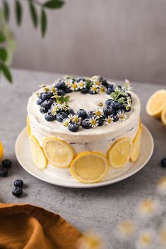 a cake with lemons, blueberries and daisies on it sitting on a plate