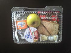 a plastic lunch box with an apple, sandwich, cheese, and other food items