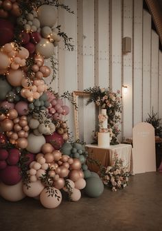 a wedding cake is surrounded by balloons and greenery on the wall in front of it