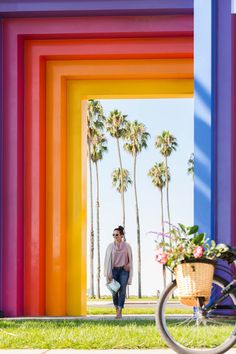 a woman walking down a street past tall colorful buildings with palm trees in the background