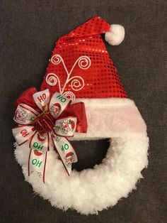 a red and white santa hat on top of a christmas wreath with a ribbon around it