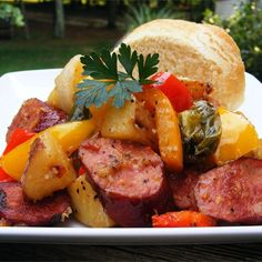 a white plate topped with meat and veggies next to a bun on a table