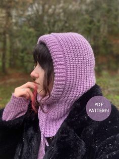 a woman wearing a purple knitted hat and black fur coat in front of trees