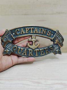 a person holding up a metal badge that says captain's quarters with an anchor on it