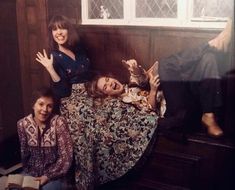 two women and a cat sitting on a bed in a room with wood paneling