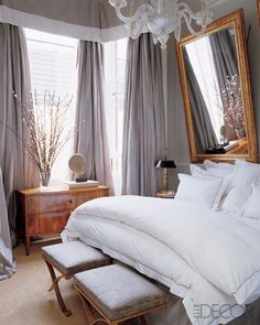 a white bed sitting in a bedroom under a chandelier next to two mirrors