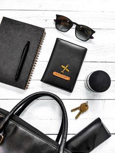 the contents of a woman's purse laid out on a white wooden table, including a notebook, pen and sunglasses