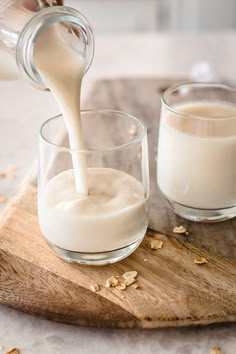 milk being poured into two glasses on a cutting board with oats scattered around it