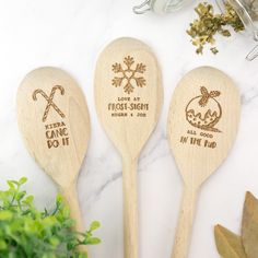 three wooden spoons with engraved designs on them sitting next to some leaves and herbs