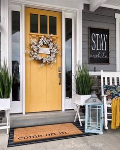 a yellow front door with a welcome mat and two white chairs on the porch next to it