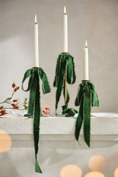 three candles are sitting on a mantle decorated with green ribbon