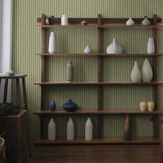 several vases are arranged on shelves in a room with green walls and wood flooring