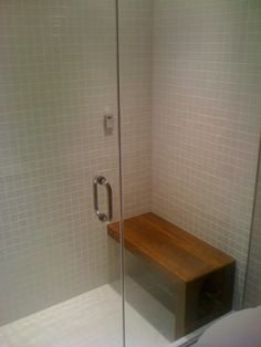 a glass shower door with a wooden bench in the corner and white tile on the walls