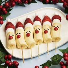 some fruit with faces on them are sitting on a white plate and surrounded by holly leaves