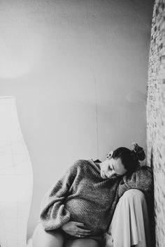 a woman sitting on top of a bed next to a brick wall with her head down