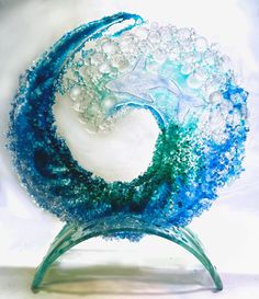 an artistic glass sculpture with blue and green swirls on it's base, against a white background