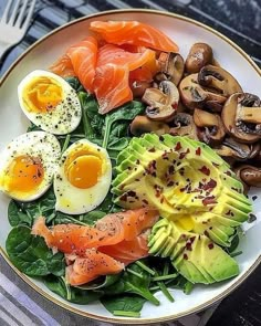 a white plate topped with eggs, salmon and avocado on top of spinach