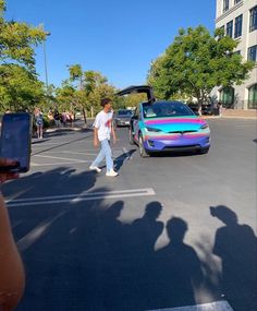 a man walking down the street next to a car with rainbow painted stripes on it