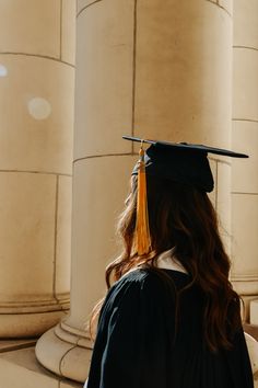 a woman wearing a graduation cap and gown standing in front of pillars with columns behind her