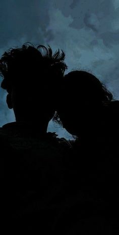 the silhouette of a man and woman kissing in front of a dark sky with clouds