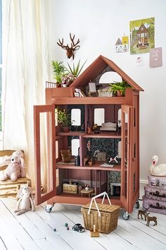 a wooden doll house sitting on top of a floor next to stuffed animals and toys