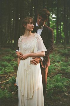 a man and woman standing next to each other in the woods