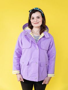 a woman standing in front of a yellow background wearing a purple jacket and black leggings