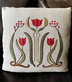 a white pillow with red flowers and green stems on the front, sitting on a black leather couch