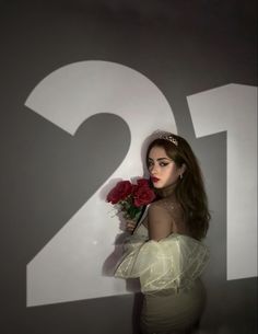 a woman in a white dress holding a bouquet of red roses and the number twenty two behind her