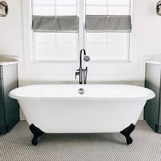 a white bath tub sitting in a bathroom next to a window with blind shades on the windowsill