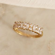 On a tan background is a gold band ring with round and baguette cz stones on the top half. Baguette Ring, Cz Stone, Gold Plating, Next Level, Sale Items, 18k Gold, Jewelry Rings, Gold Plate, The Next